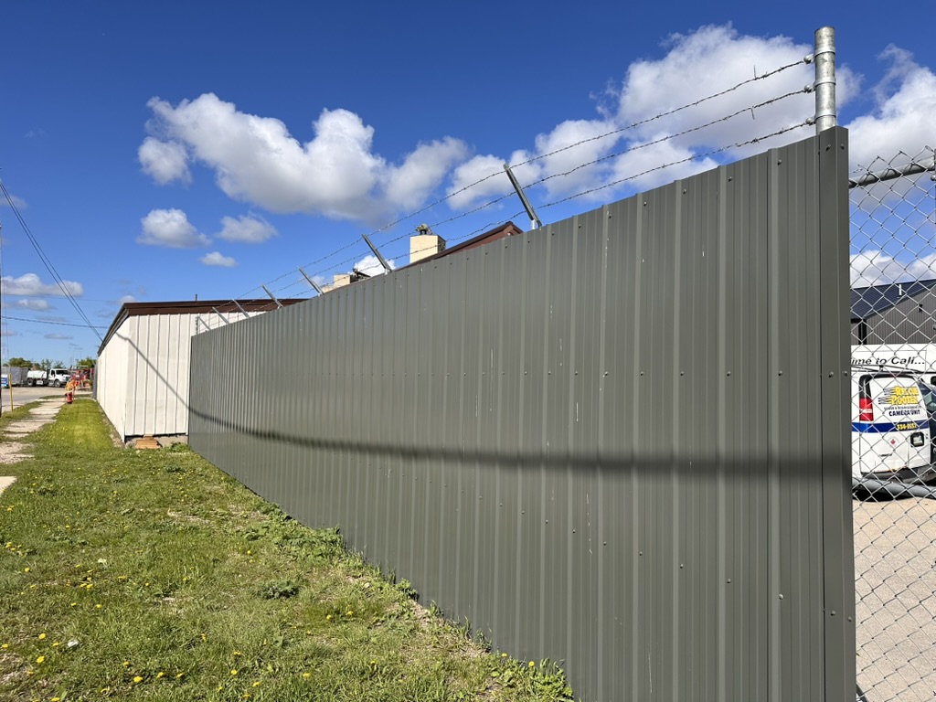Commercial sheet metal privacy fence with barbed wire